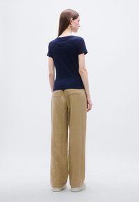 Μπλε ναυτικό T-shirt με κοντό μανίκι και στρογγυλή λαιμόκοψη, συνδυασμένο με χαλαρά, ανοιχτό καφέ παντελόνια με πίσω τσέπες και άνετη εφαρμογή.