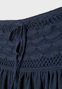 Dark navy blue crochet fabric with leaf patterns, a tied drawstring, and fringed edges.