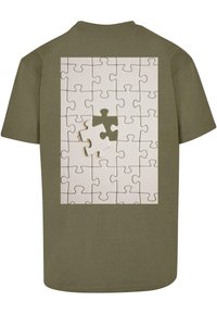 Oliven grøn T-shirt med et puslespil grafik på bagsiden, bestående af sammenflettede hvide brikker og en grå brik.