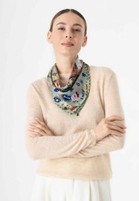 Zijden sjaal met een groen en bloemig patroon, voorzien van kleurrijke accenten. Driehoekige vorm gedrapeerd om de hals, aangevuld met een gestructureerde beige trui.