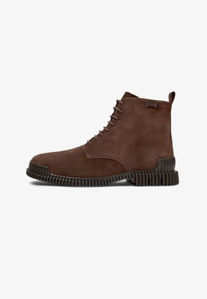 Botines de ante marrón con suela de goma texturizada, diseño de cordones minimalista y un destacado logotipo de la marca en el lateral.