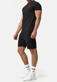 Sort atletisk t-shirt og shorts lavet af glat stof. Kombineret med hvide sneakers og stribede ankelstrømper, der viser et sporty look.