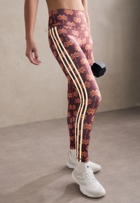 Leggings i bourgogne grundfärg med tropiskt palmmönster i orange och krämfärgade sidostråk. Materialet är elastiskt och åtsittande.