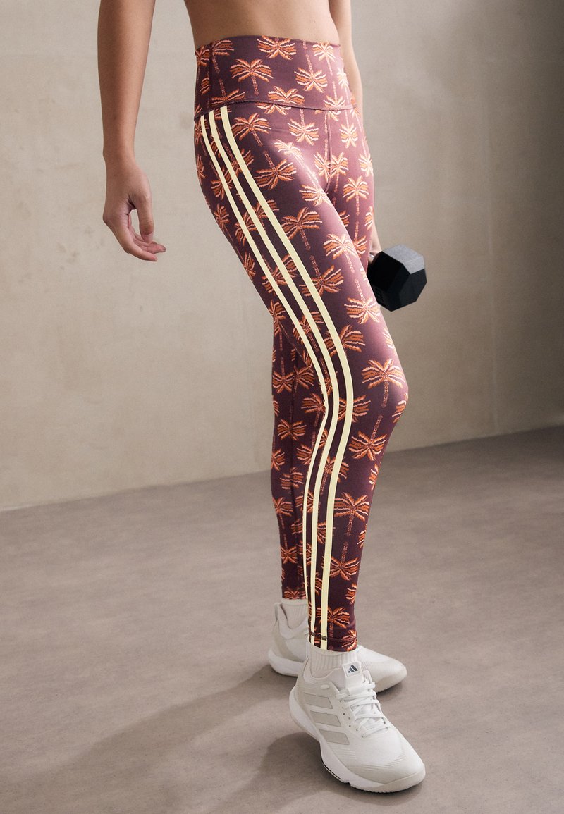 Leggings i bourgogne grundfärg med tropiskt palmmönster i orange och krämfärgade sidostråk. Materialet är elastiskt och åtsittande.