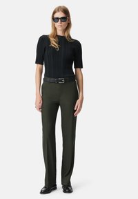 Zwarte geribbelde top met korte mouwen, groene op maat gemaakte broek, zwarte riem met zilveren gesp, en zwarte rechthoekige zonnebril. Gladde textuur, getailleerd ontwerp.