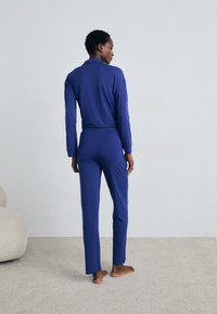 Dvivietis naktinis kostiumas, pagamintas iš sodrios mėlynos spalvos, su ilgomis rankovėmis marškinėliais ir pritaikytais keliais, pagamintas iš minkštos, elastingos medžiagos.