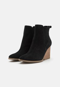 Botas de ante negras hasta el tobillo con diseño de punta afilada, paneles laterales elásticos y un tacón de madera apilada. Las suelas de goma ofrecen agarre y estabilidad.