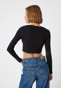 Top cropped nero a maniche lunghe con texture a coste, abbinato a jeans in denim blu a vita alta con un classico design a cinque tasche.