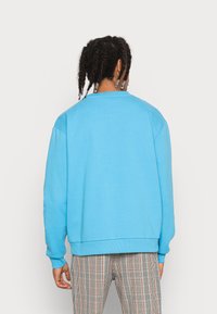 Sweatshirt blu brillante con scollatura rotonda e orlo a coste. Presenta una vestibilità comoda e spalle scese, abbinato a pantaloni a quadri.