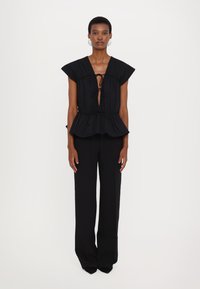Schwarzes Peplum-Oberteil mit kurzen Ärmeln, tiefem V-Ausschnitt und Bindeband. Kombiniert mit hoch sitzenden schwarzen, weit geschnittenen Hosen aus einem glatten Stoff.