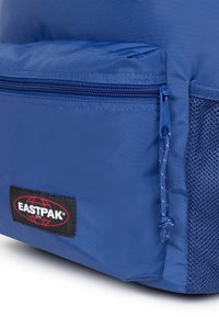 Blå nylonryggsäck med ett huvudfack med dragkedja, sidofack i mesh och en svart Eastpak-logotyp på framsidan.