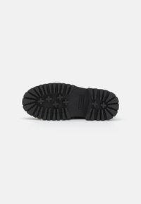 Black rubber shoe sole with thick tread pattern and cross-shaped lugs, designed for traction and durability. Smooth finish with reinforced edges.