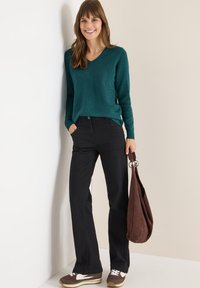 Suéter de pico en color verde azulado, jeans negros, bolso de ante marrón y zapatillas marrones con detalles en blanco. Textura suave y corte relajado.