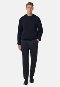 Námořnický pletený svetr s žebrovanou texturou, spárovaný s námořnickými skládacími kalhotami. Outfit doplňují černé sportovní boty.