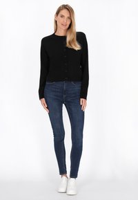 Mustat lyhyet neuletakit, joissa on pyöreä kaula-aukko, nappisuljenta ja pitkät hihat, yhdistettynä tummiin slim fit -farkkuihin ja valkoisiin lenkkareihin.