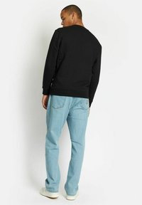 Svart genser med rund hals, parret med lyseblå jeans. Stoffet ser glatt ut, med ribbede mansjetter og linning.