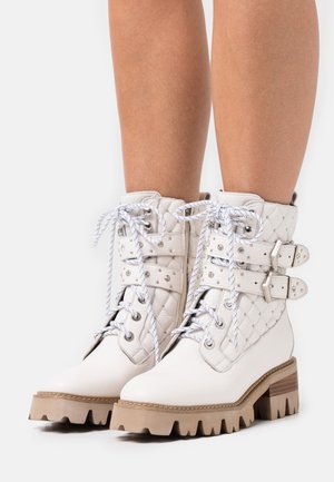 Botas blancas hasta el tobillo con diseño acolchado, remaches decorativos y acentos de hebilla plateada. Presenta punta redonda y suela de plataforma gruesa.