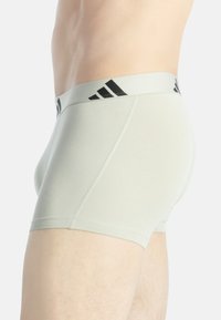 Světlé šedé boxerky s černým elastickým pasem a třemi černými pruhy, vyrobené z měkké tkaniny s hladkou texturou.