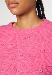 Pull en tricot rose avec un col rond, un motif texturé et des détails à maille ouverte. Matière douce avec un aspect légèrement duveteux.