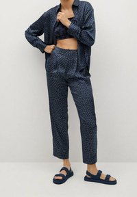 Person, der eine passende dunkelblaue gemusterte Jacke und Hose, ein kurzes Oberteil und navyblaue Sandalen mit Riemen trägt.