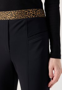 Leggings de sport noirs avec une ceinture imprimée léopard, présentant une texture lisse et des poches latérales pour plus de fonctionnalité.