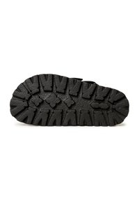 Suela de zapato de goma negra con patrones de relieve profundos y formas variadas, que ofrecen tracción y durabilidad. Superficie texturizada con un acabado mate.