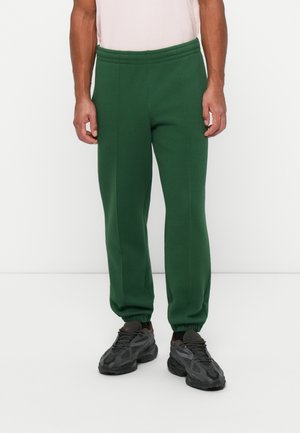 Green sweatpants with elastic waistband and cuffs, made of soft fabric. Straight-leg design with minimal seam detailing. Worn with black sneakers.