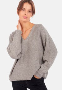 Pull gris, oversize en col V fabriqué en maille douce. Présente des manches longues légèrement bouffantes et une coupe décontractée avec des poignets côtelés.