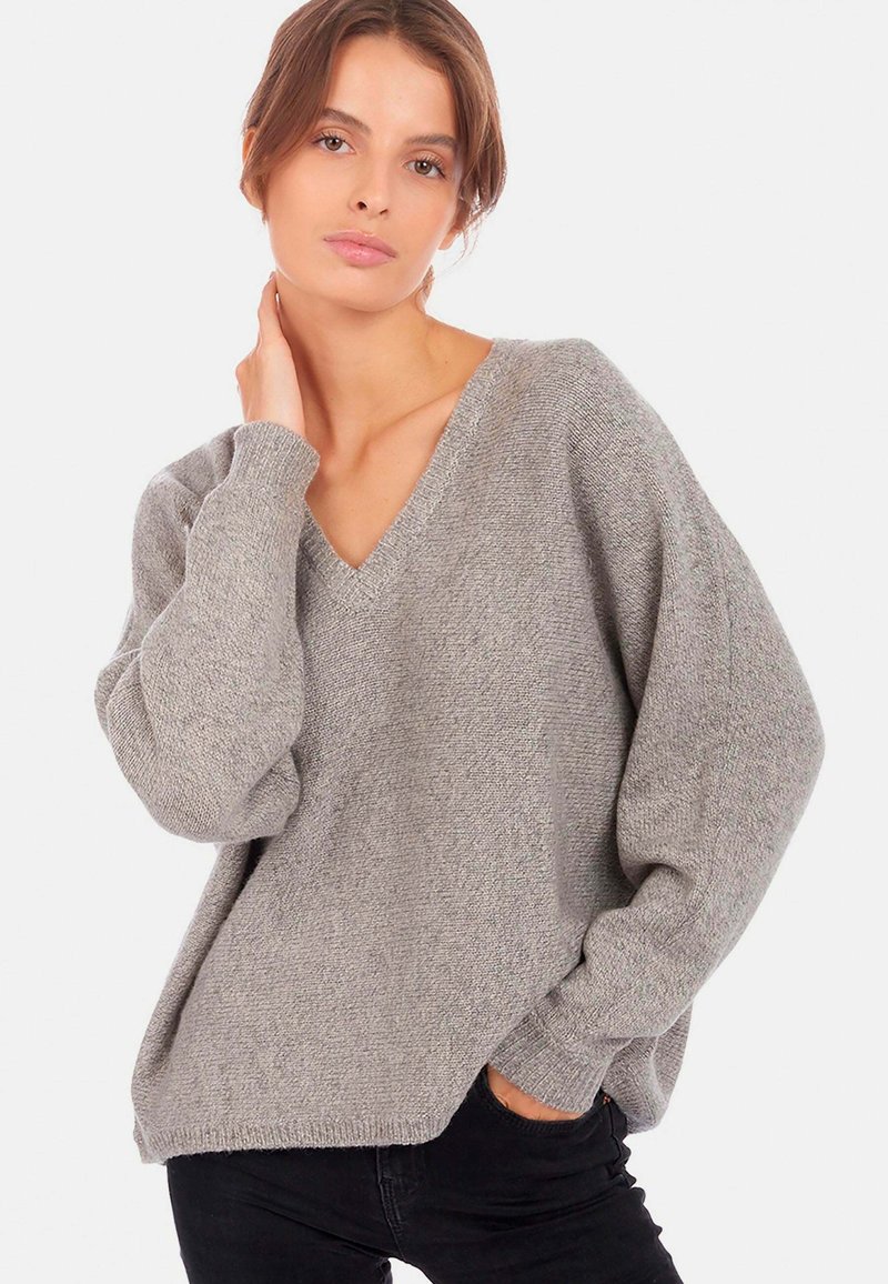 Pull gris, oversize en col V fabriqué en maille douce. Présente des manches longues légèrement bouffantes et une coupe décontractée avec des poignets côtelés.