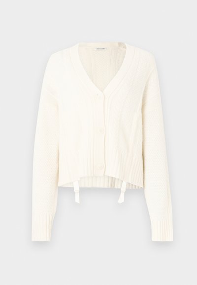 Bílý svetr s copánkovým vzorem, véčkovým výstřihem, pěti knoflíky, žebrovanými manžetami a krátkým střihem se dvěma šňůrkami na spodním lemu.