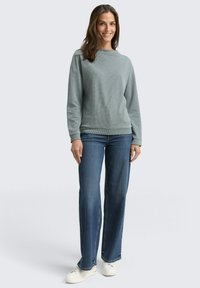 Light grey textured sweatshirt with long sleeves, paired with straight-leg blue jeans and white sneakers. Simple, casual design.