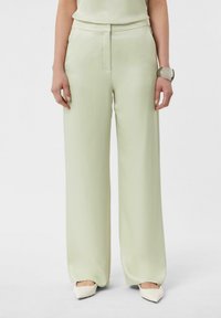 Jasnozielone szerokie spodnie z gładkiego materiału, z dopasowanym stanem i kieszeniami bocznymi, zestawione z białymi, spiczastymi butami.