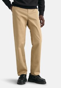 Khaki trousers made of cotton, straight-leg design, featuring a smooth texture. Paired with black shoes and a black sweatshirt.