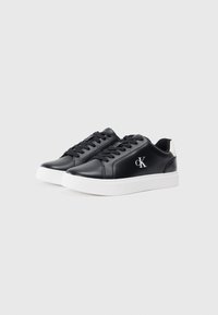 Sneakers negre din material sintetic, cu talpă din cauciuc alb, dotate cu șiruri plate, detaliu logo pe lateral și accent contrastant la călcâi. Textură netedă.