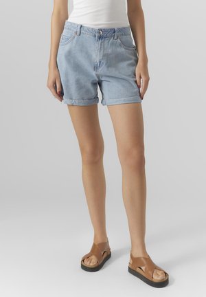 Pantalones cortos de mezclilla azul claro con dobladillos enrollados, dos bolsillos laterales y cierre de botón, combinados con sandalias marrones de tiras con suela de plataforma.