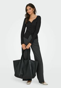 Czarny, długi kardigan na guziki, w połączeniu z spodniami w cienkie prążki, trzymający dużą czarną torbę typu tote. Beżowe baleriny dopełniają strój.