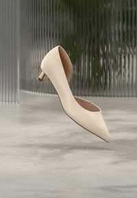 Μπεζ γόβα με μυτερή μύτη, λείο υλικό από συνθετικό δέρμα και λεπτή, μικρή φιάπα. Μινιμαλιστικός σχεδιασμός με χαμηλό κόψιμο στα πλάγια.