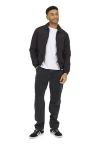 Giubbotto bomber leggero nero con colletto, abbinato a una maglietta bianca, jeans neri e sneaker nere con strisce bianche.