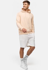 Sudadera de melocotón claro con cordones ajustables, combinada con shorts blancos. Los accesorios incluyen zapatillas blancas y calcetines deportivos a rayas.