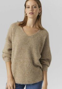 Beige stickad tröja med V-ringning, ribbad textur och löst sittande långa ärmar. Tillsammans med blå jeans ger den ett mjukt och mysigt utseende.