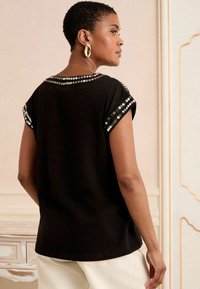 T-shirt noir à manches courtes repliées avec des sequins argentés le long de l'encolure et des bords des manches. Texture lisse, coupe décontractée.