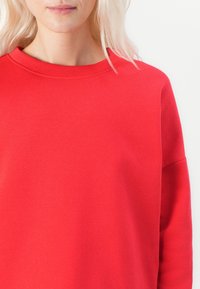 Sweat-shirt rouge en coton lisse avec un col rond et des épaules tombantes, présentant un design épuré et uni.