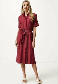Abito camicia color borgogna con maniche corte, vita regolabile con un fiocco e chiusura a bottoni sul davanti. Realizzato in tessuto leggero, arriva poco sotto il ginocchio.
