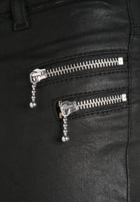 Tecido de denim negro com dois bolsillos com zíper y herrajes de plata, presentando un acabado suave y texturizado.