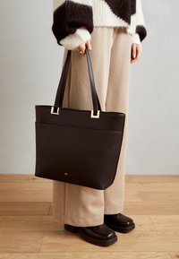 Czarna torba tote z sztucznej skóry z złotymi akcentami i dwoma ramiączkami; charakteryzuje się eleganckim, prostokątnym kształtem i minimalistycznym logo.