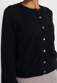 Czarny dziany kardigan z długimi rękawami i okrągłym dekoltem. Zawiera sześć guzików z przodu, gładką teksturę i dopasowaną talię.