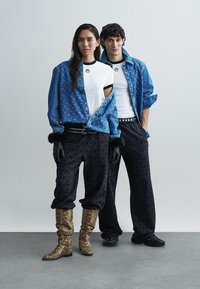 Denimtakki aaltoilevalla kuviolla, musta logolla varustettu t-paita, löysät mustat kuvioidut housut ja käärmekuvioiset saappaat. Hansikkaat ja niiteillä koristeltu vyö.