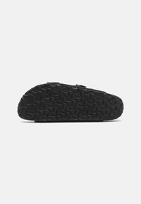 Svart slip-on sko med en texturerad gummisula som har ett vågigt mönster. Minimalistisk design utan synlig hårdvara eller utsmyckningar.