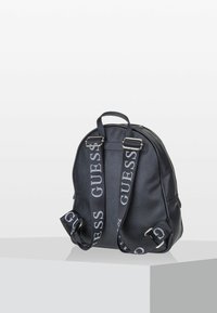 Sac à dos en cuir noir avec surface texturée, bretelles réglables avec logo et poignée supérieure. Forme arrondie avec fermeture zippée.