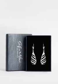 Silver droppformade örhängen med en vriden design och svarta ränder samt klara kristallaccenturer, presenterade i en blå sammetfodrad box.